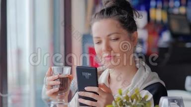 漂亮的女人在咖啡馆里用手机端着一杯热巧克力短信